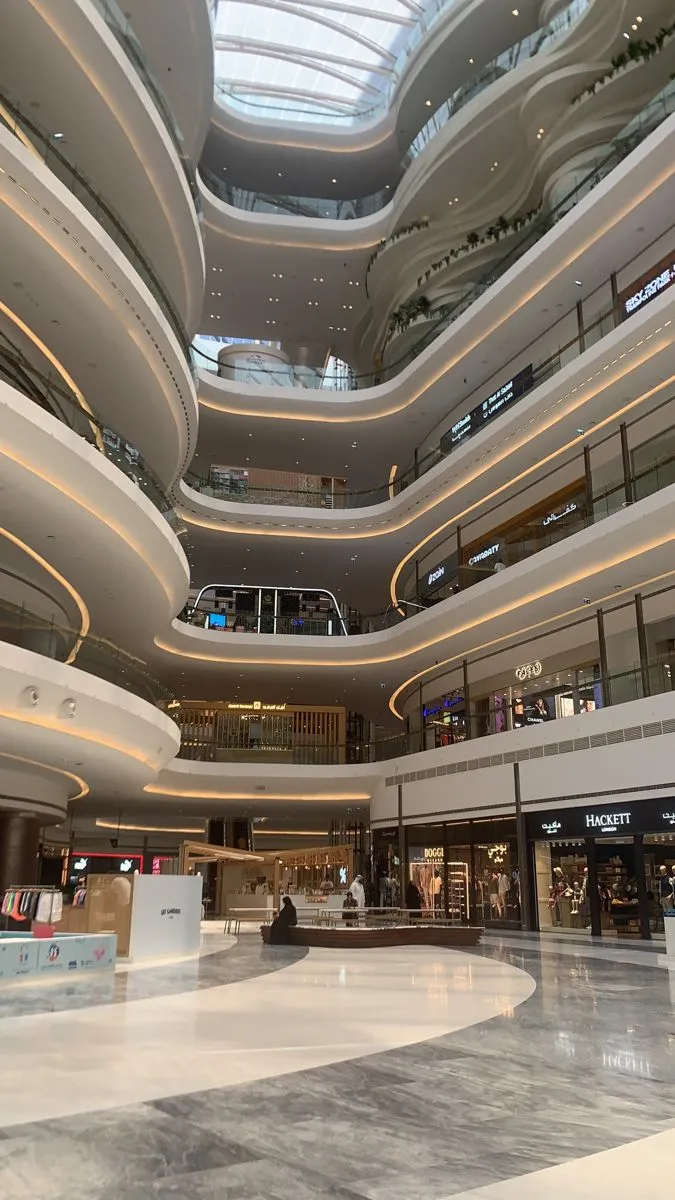 A bright multi-level shopping mall atrium with curved balconies and a glass roof