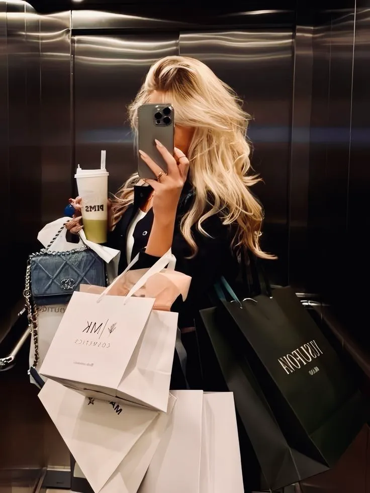 A shopper taking a mirror selfie while carrying several branded shopping bags