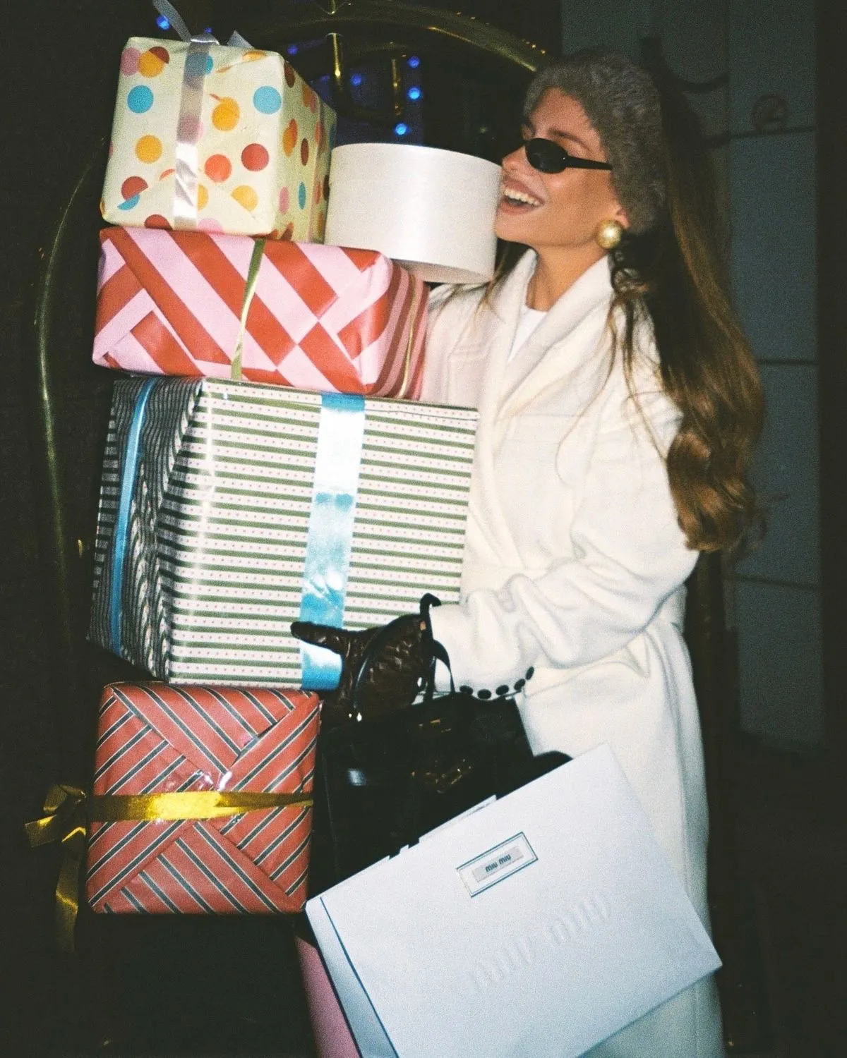 A smiling shopper carrying a tall stack of wrapped gift boxes and a shopping bag