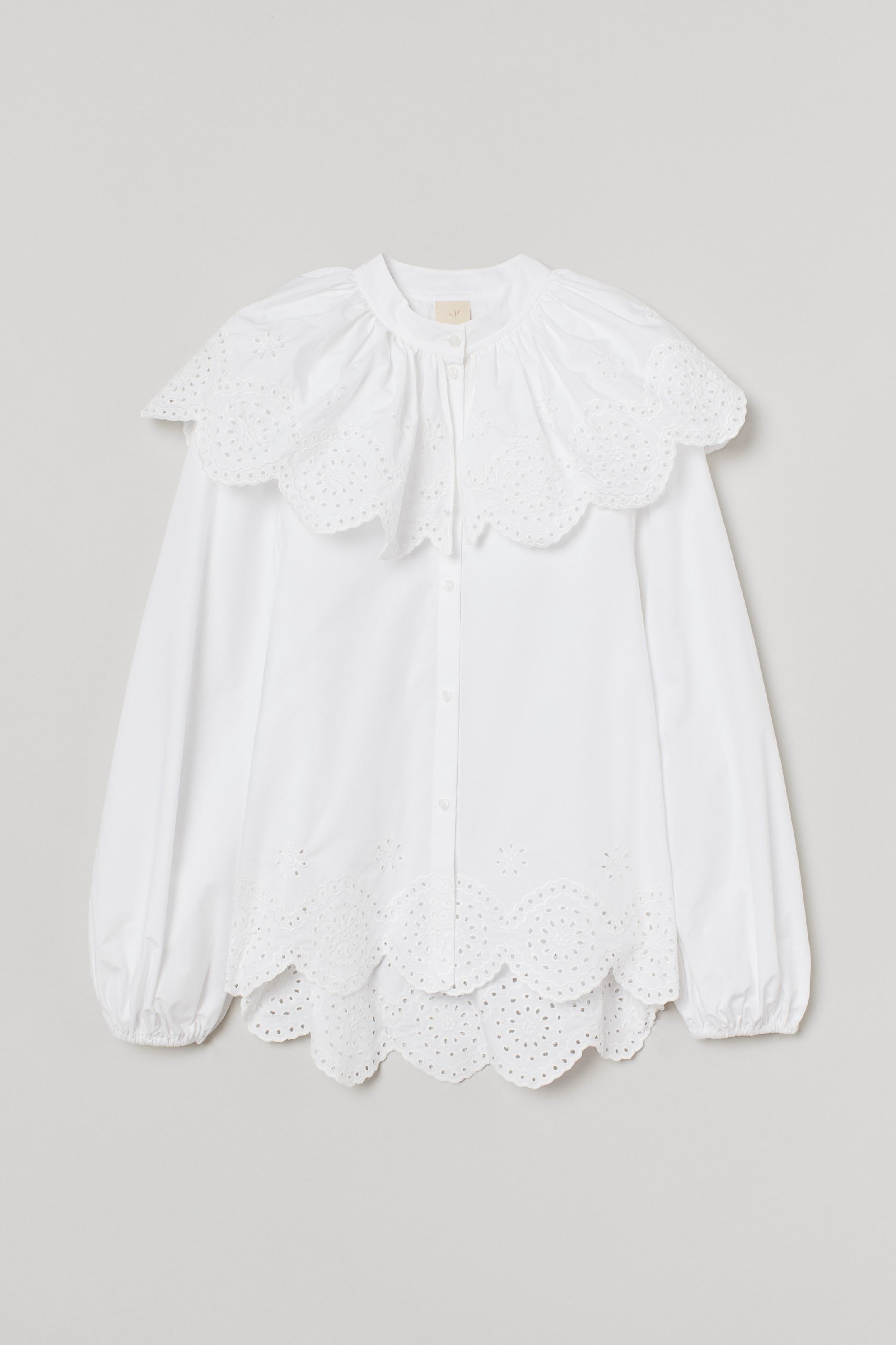 Wide cotton blouse with English embroidery, short turtleneck with semi-loose layer covering the shoulders. Buttons in front, long balloon sleeves with fine elastic lining on the cuffs and scalloped hem.