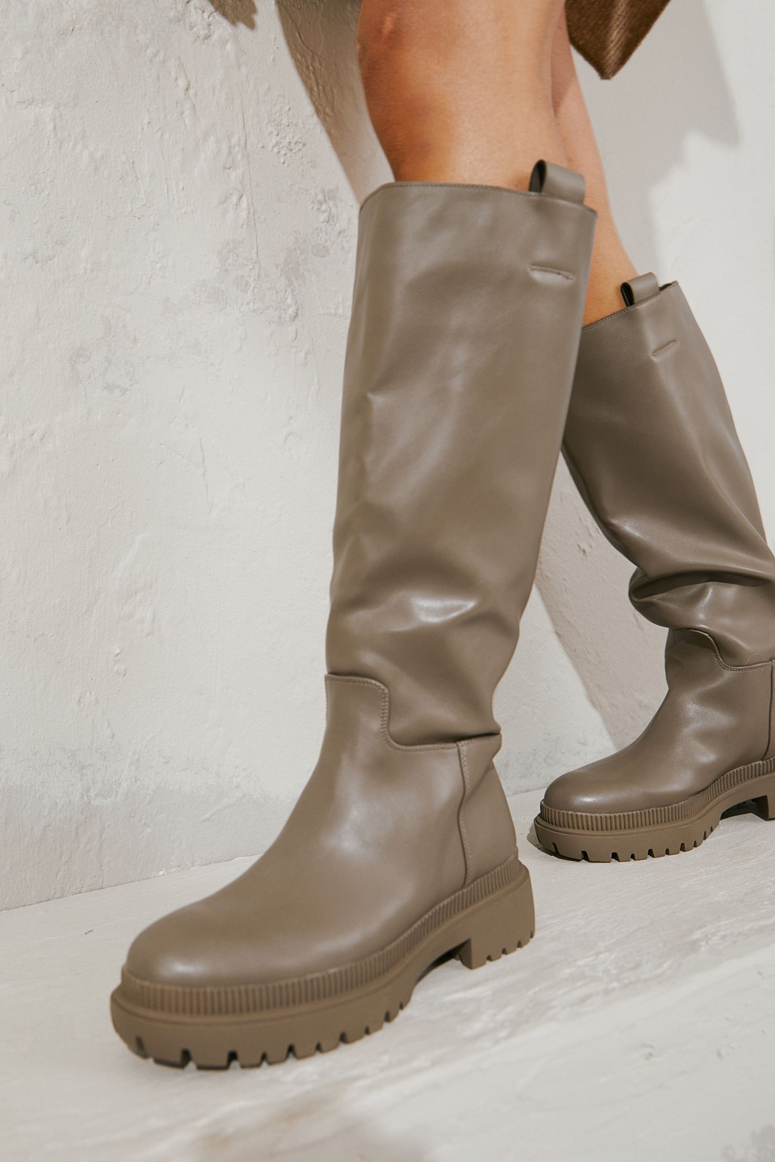 Knee boots in faux leather with side straps. Satin lining and synthetic leather insole. Thick sole with design. Heel 5,5 cm.